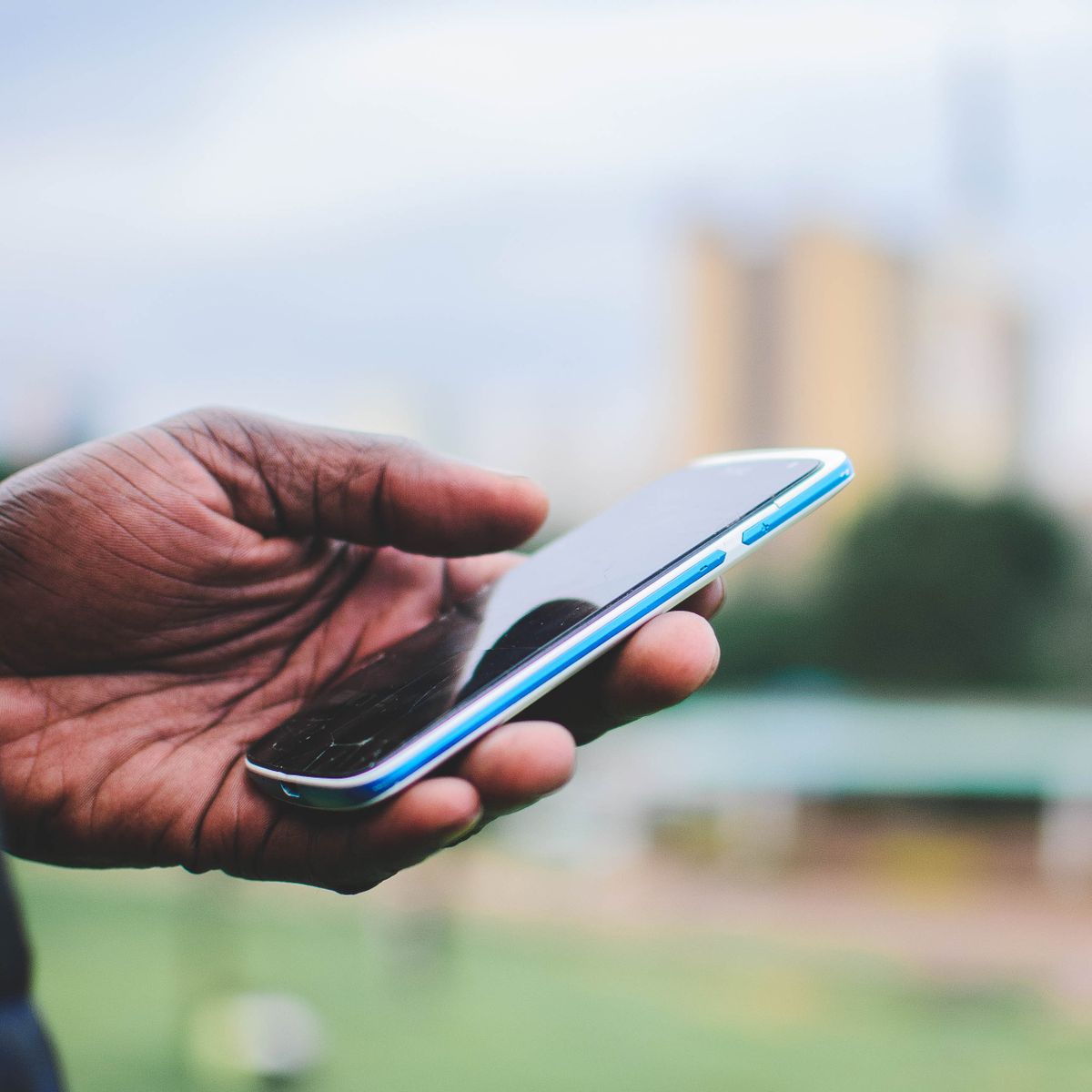 Une main tient un smartphone en extérieur pour passer un appel d'urgence